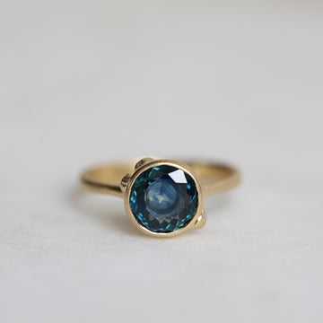 Gold ring with a blue gemstone on a light gray background