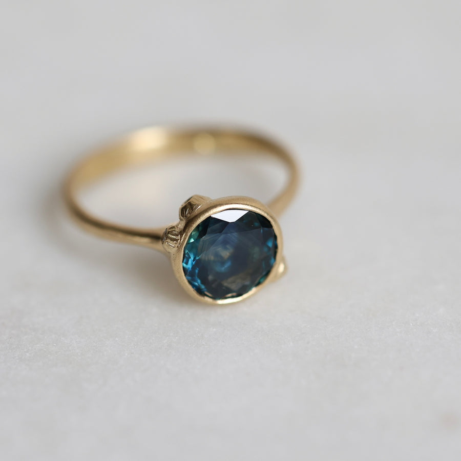 Gold ring with a blue gemstone on a light gray background