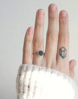 Hand wearing a gold ring with a blue stone on a plain background