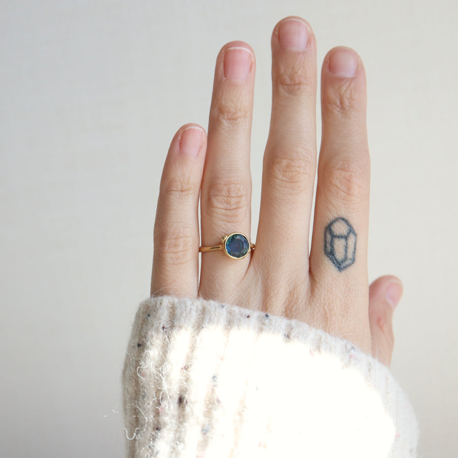 Hand wearing a gold ring with a blue stone on a plain background