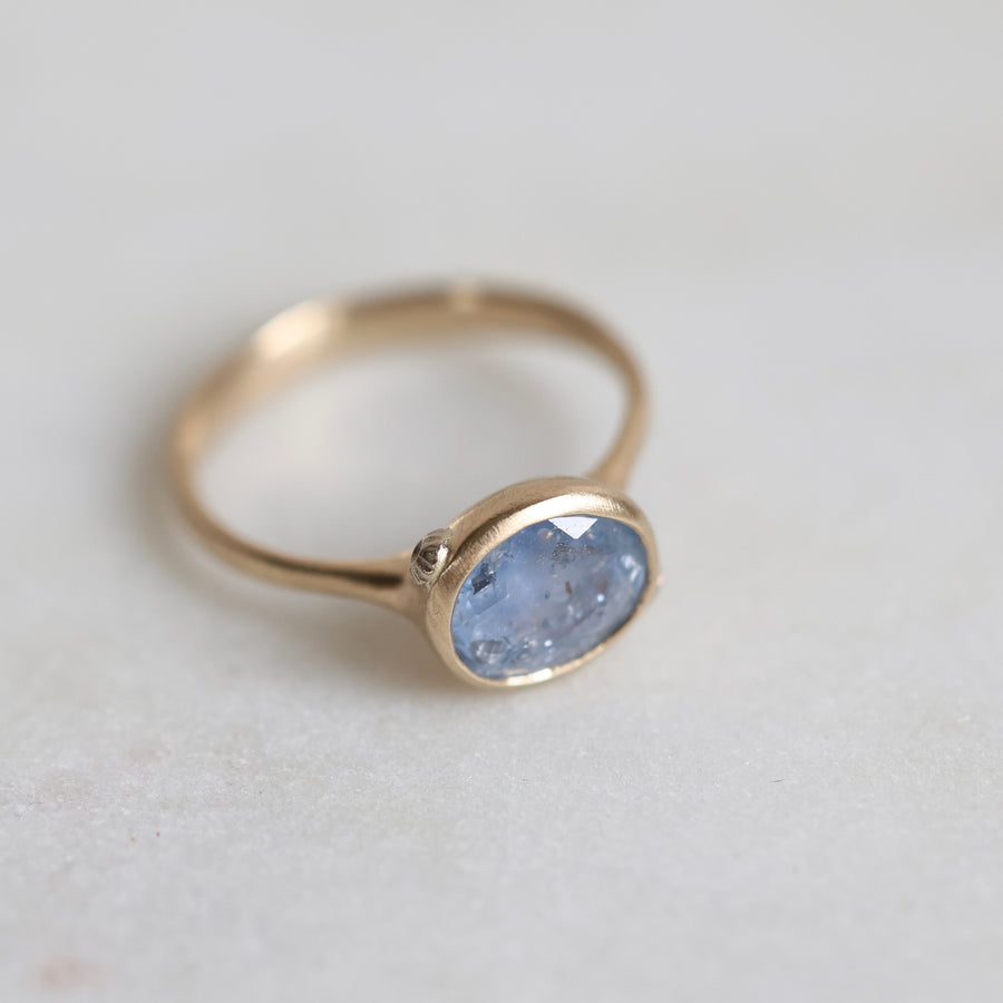 Gold ring with a blue gemstone on a light gray background