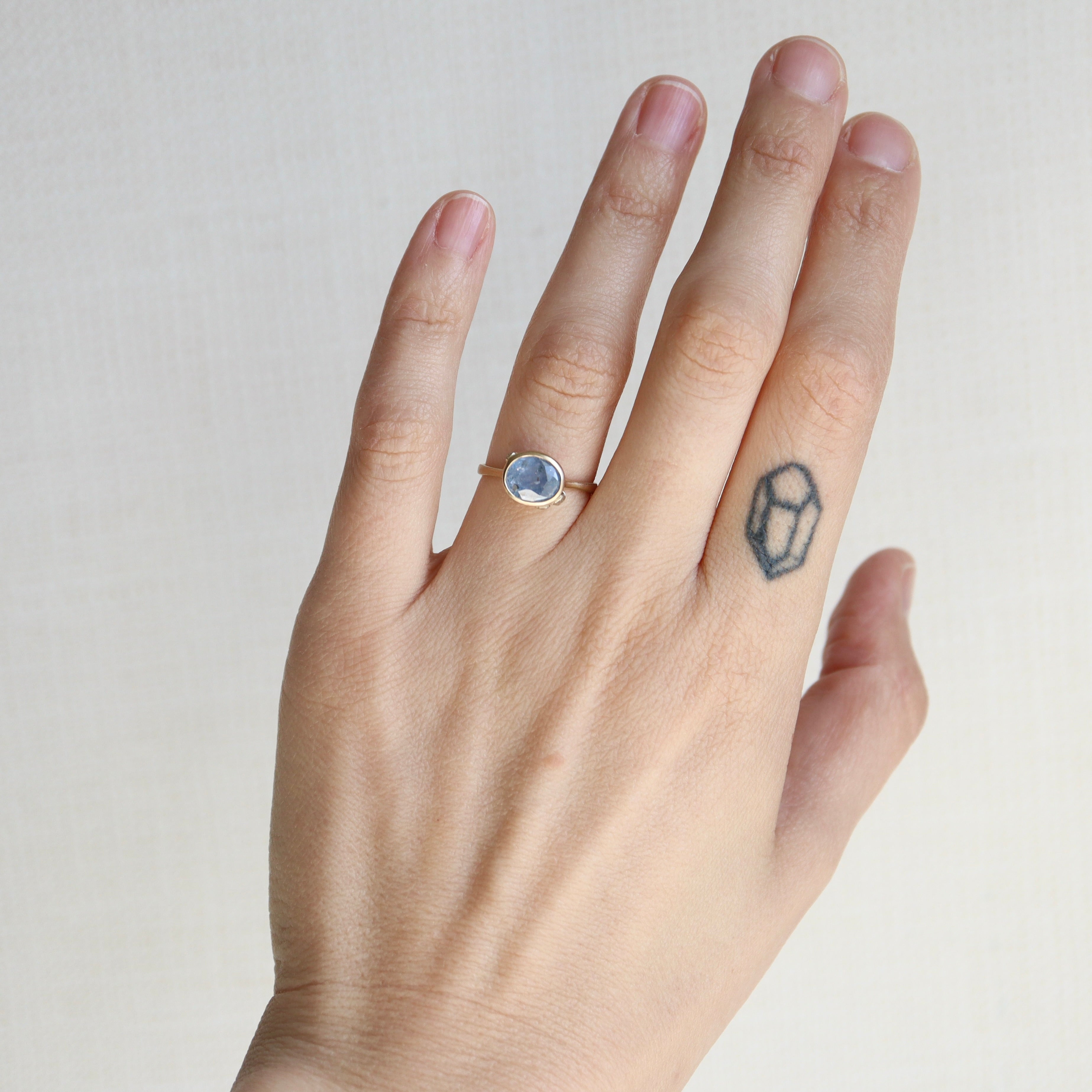 Hand wearing a ring with a gemstone on a plain background