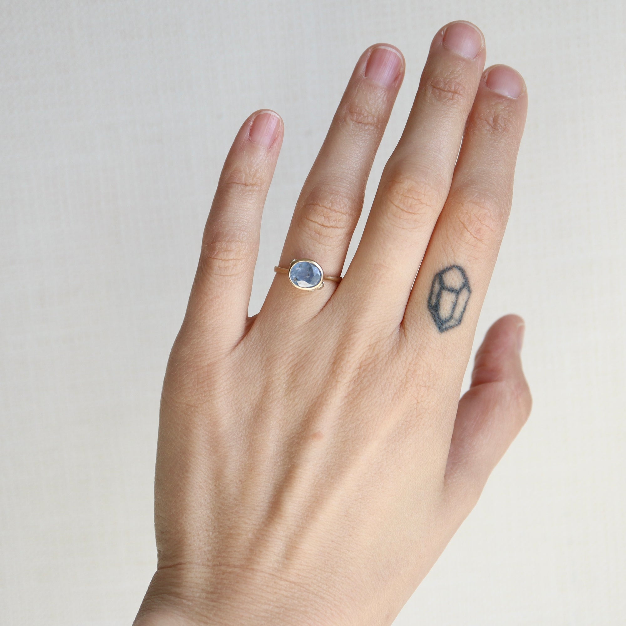 Hand wearing a ring with a gemstone on a plain background