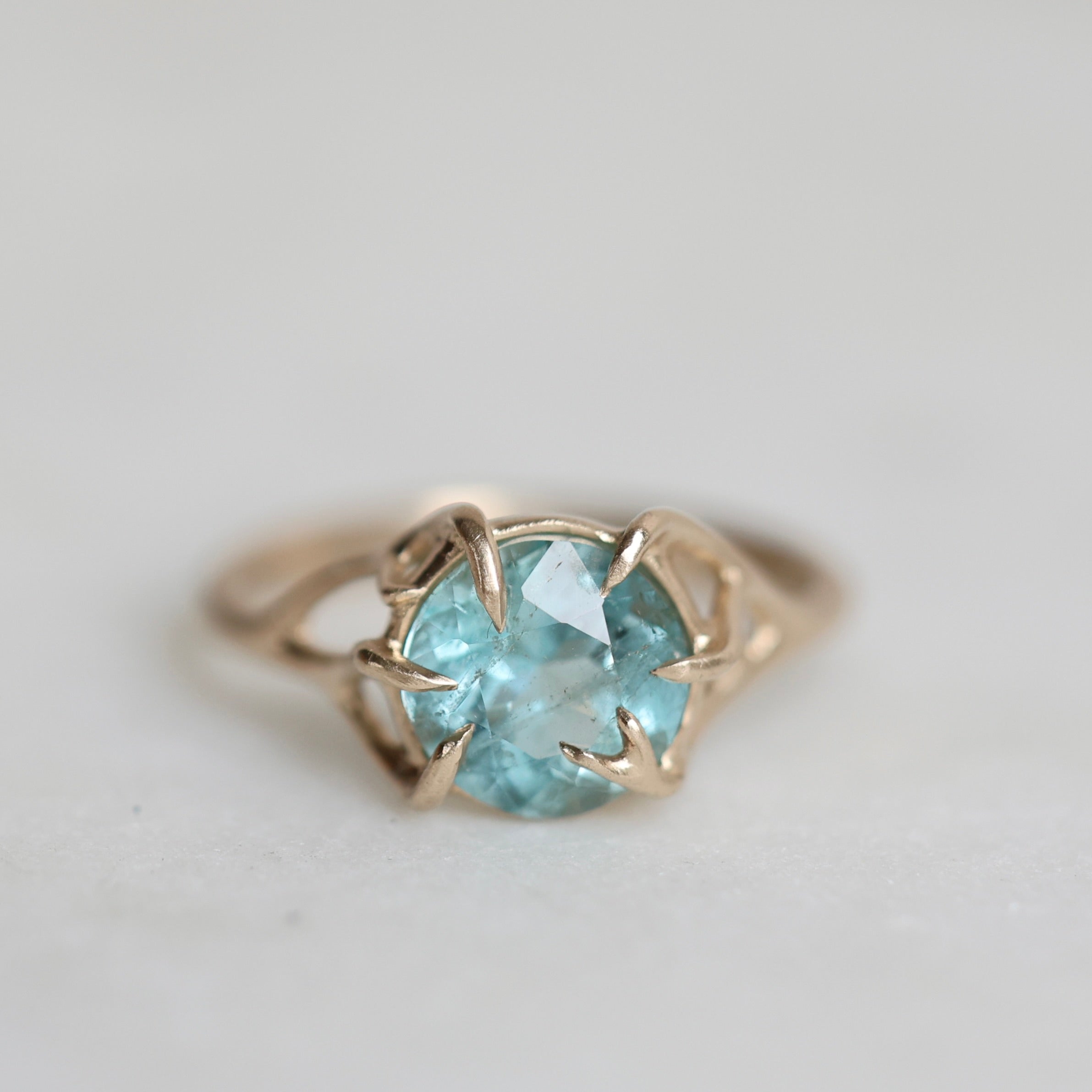 Gold ring with a blue gemstone on a light gray background