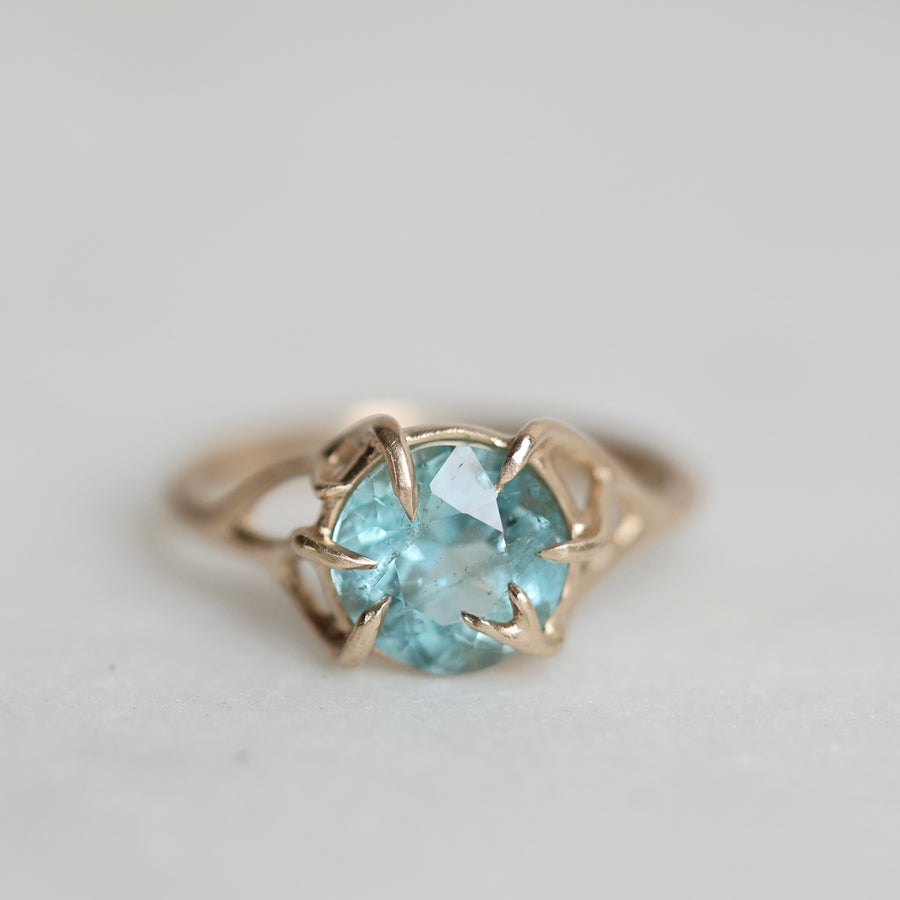 Gold ring with a blue gemstone on a light gray background