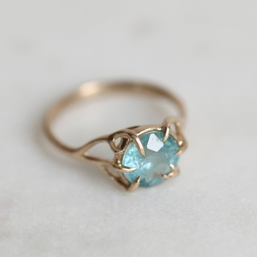 Gold ring with a blue gemstone on a light gray background