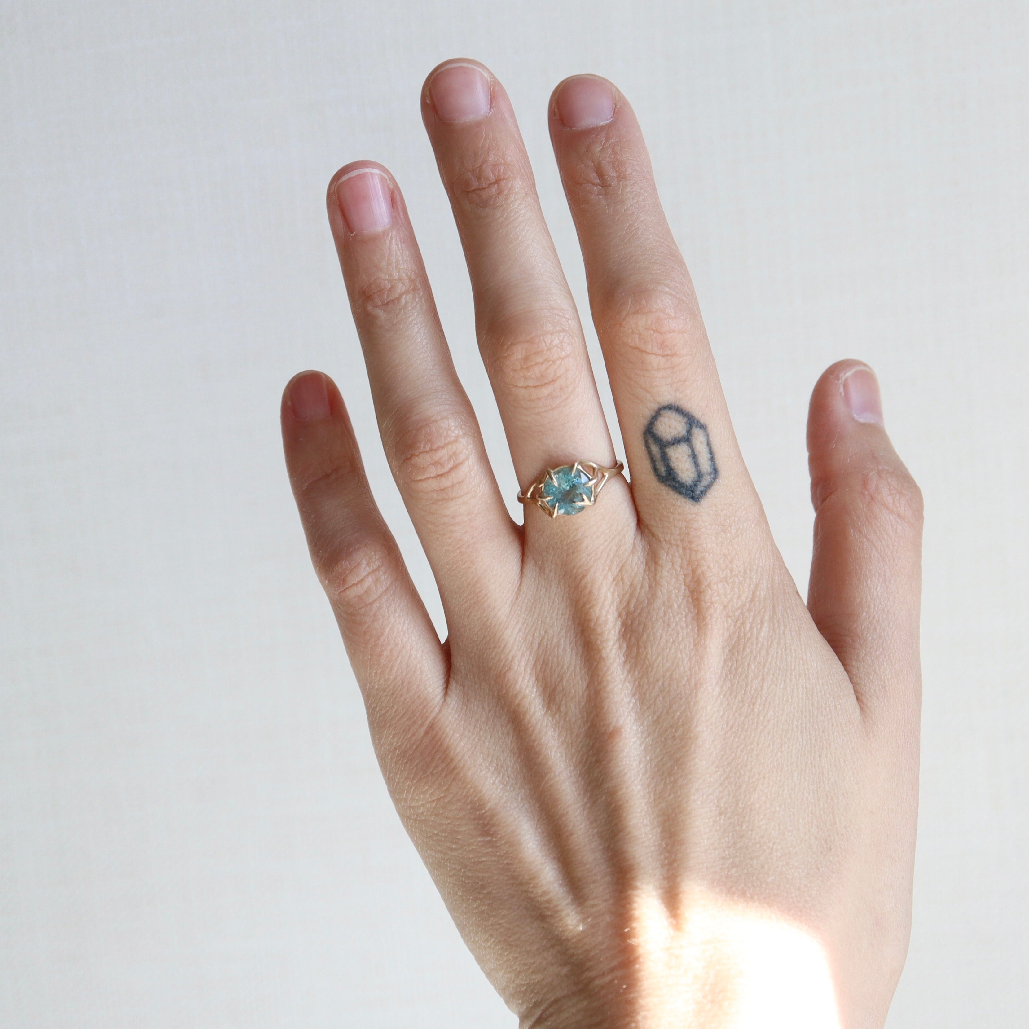 Hand wearing a ring with a blue gemstone on a plain background