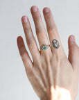 Hand wearing a ring with a blue gemstone on a plain background