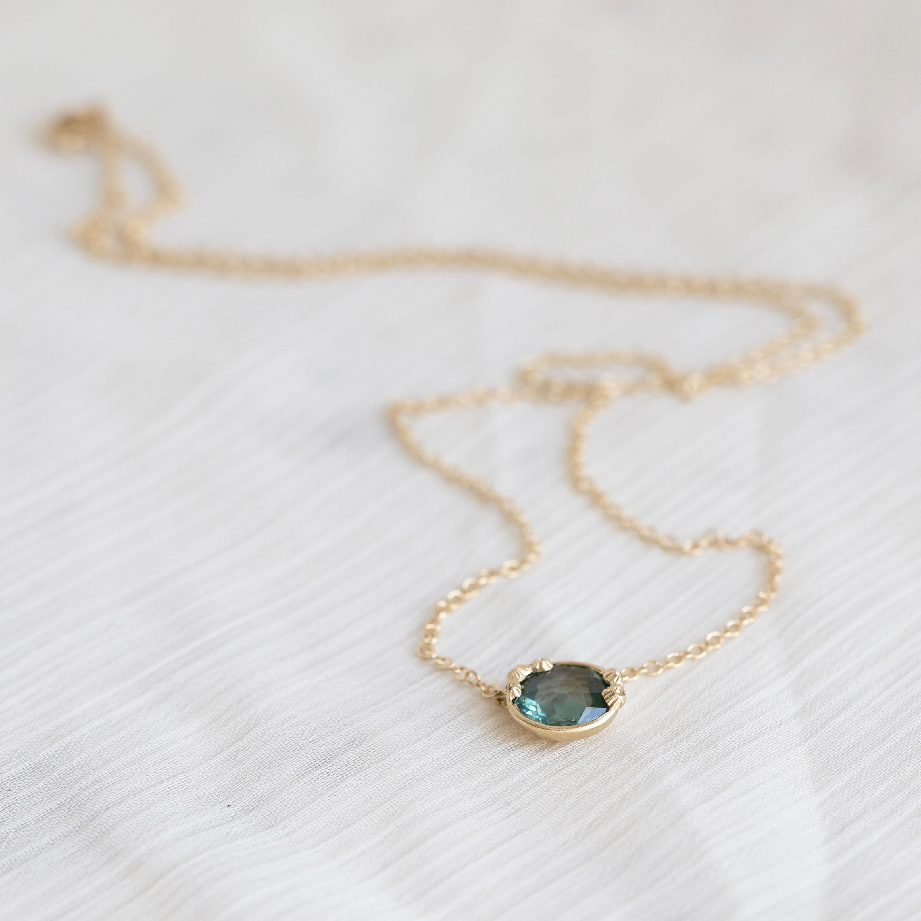 Necklace with a teal gemstone pendant on a white fabric background
