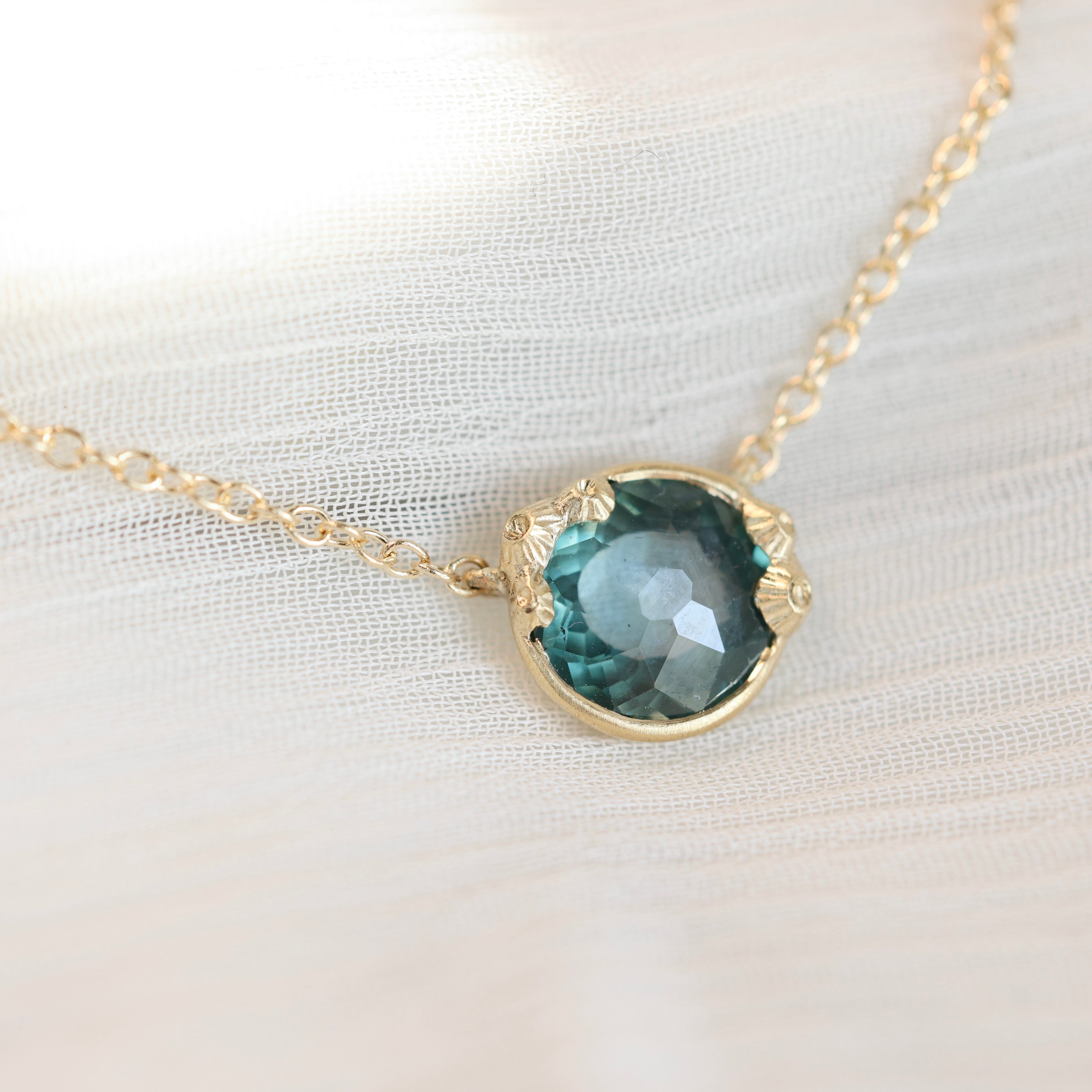 Necklace with a teal gemstone pendant on a white fabric background