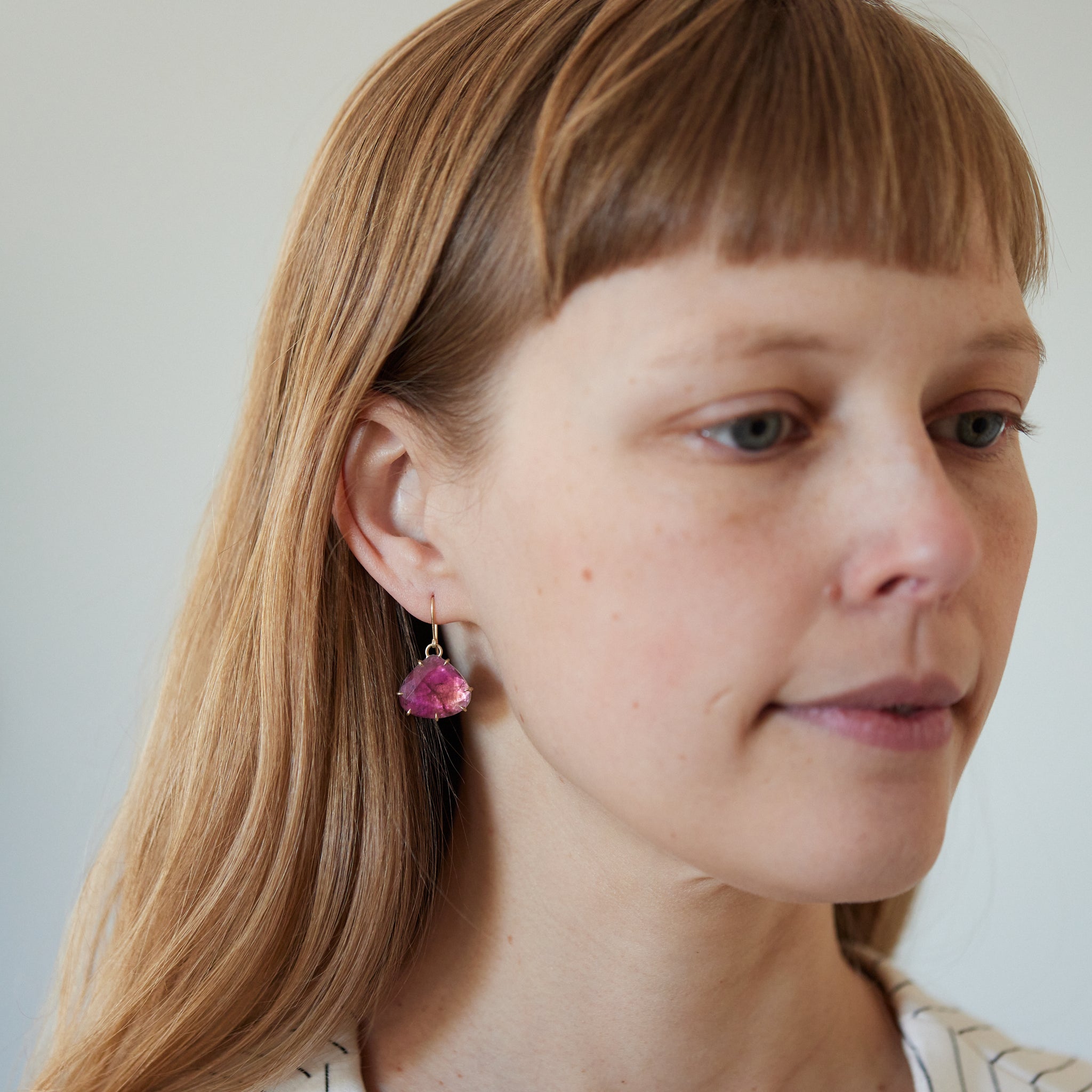 Teardrop berry tourmaline gemstones are set in gold prong with gold ear wires. Photographed on person.
