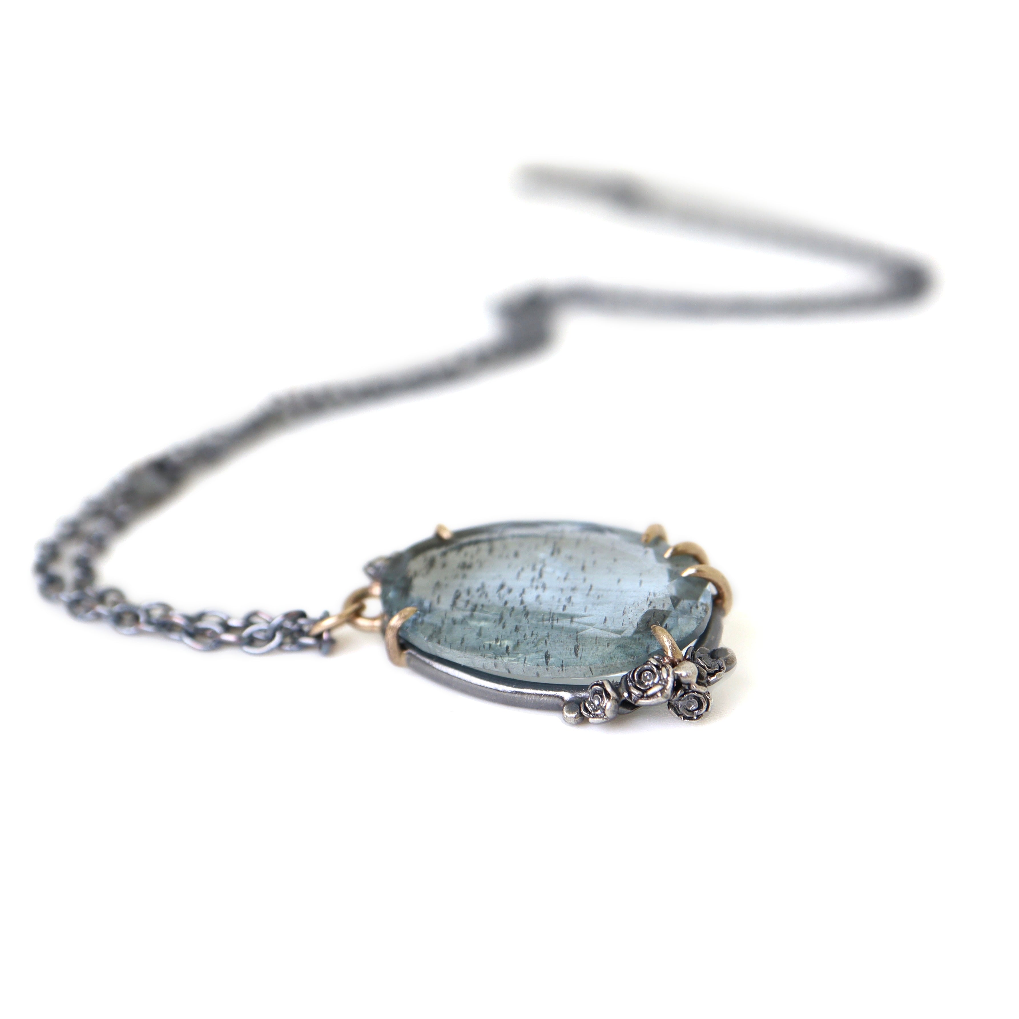 oval cool moss aquamarine sits in gold prongs with black and roses and chain.