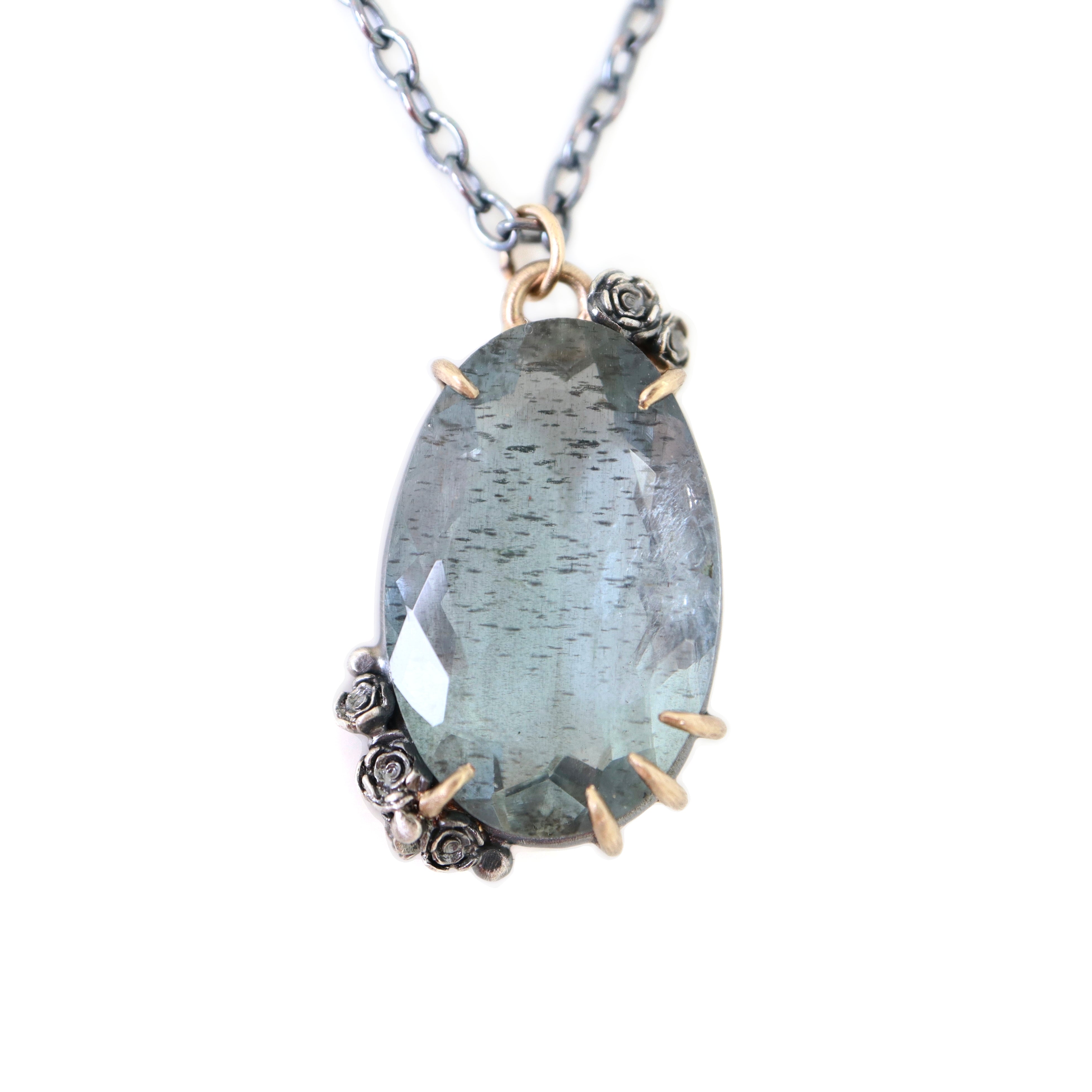 oval cool moss aquamarine sits in gold prongs with black and roses and chain.
