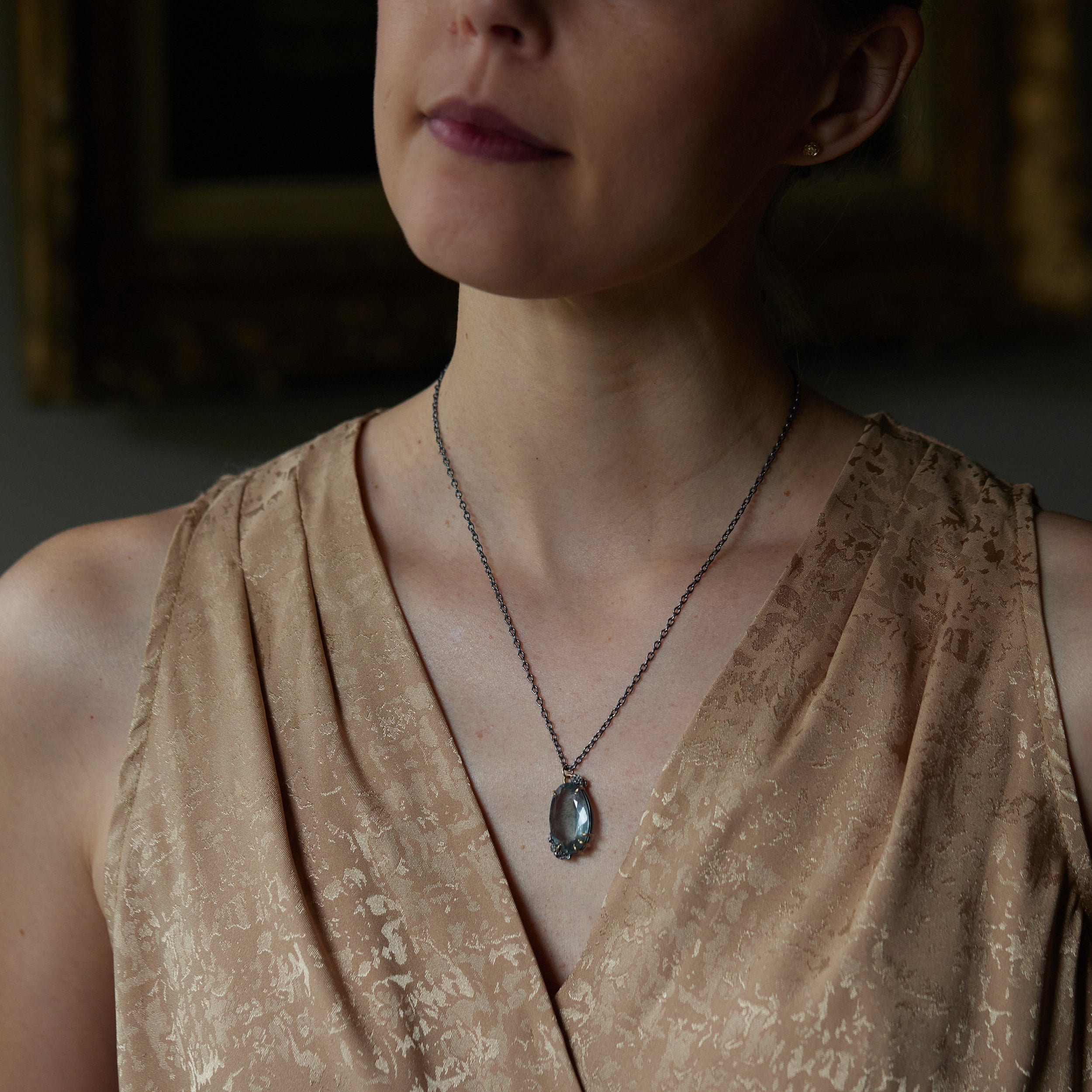 oval cool moss aquamarine sits in gold prongs with black and roses and chain. Shown on person.