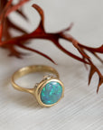Gold ring with a blue opal gemstone on a textured surface with red leaves in the background