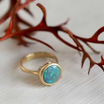 Gold ring with a blue opal gemstone on a textured surface with red leaves in the background