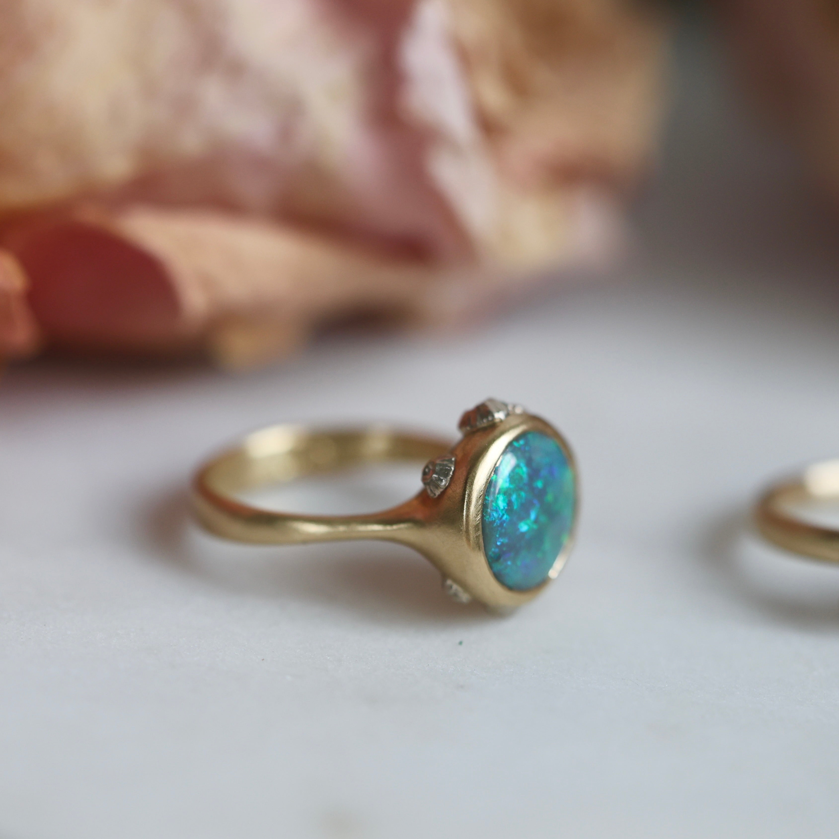 Gold ring with a blue opal on a light background with flowers in the background