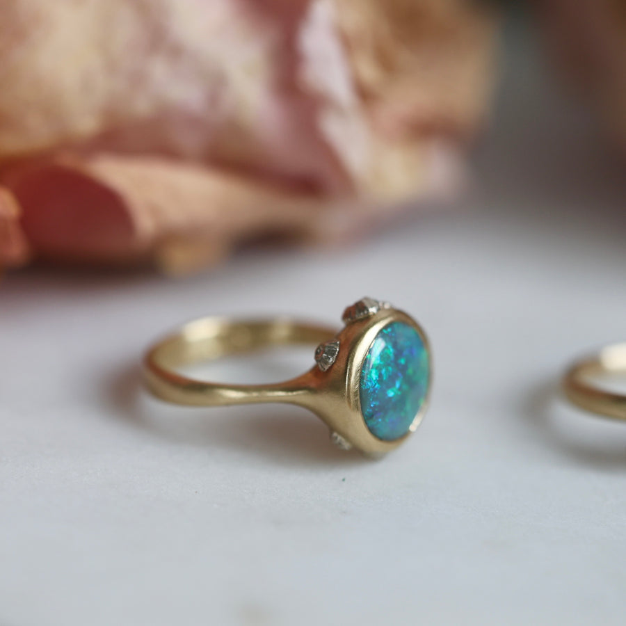 Gold ring with a blue opal on a light background with flowers in the background