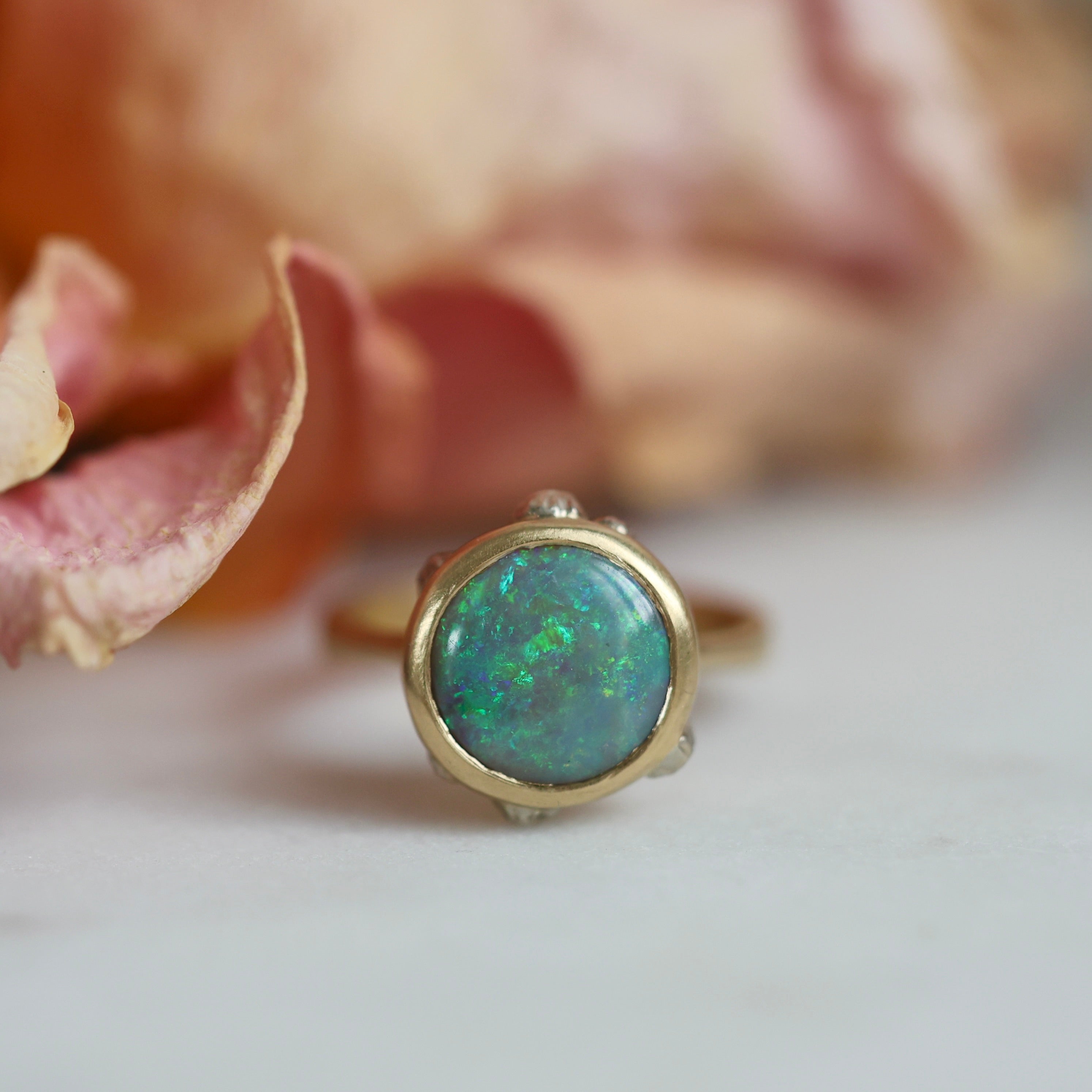 Gold ring with a green gemstone next to a pink flower