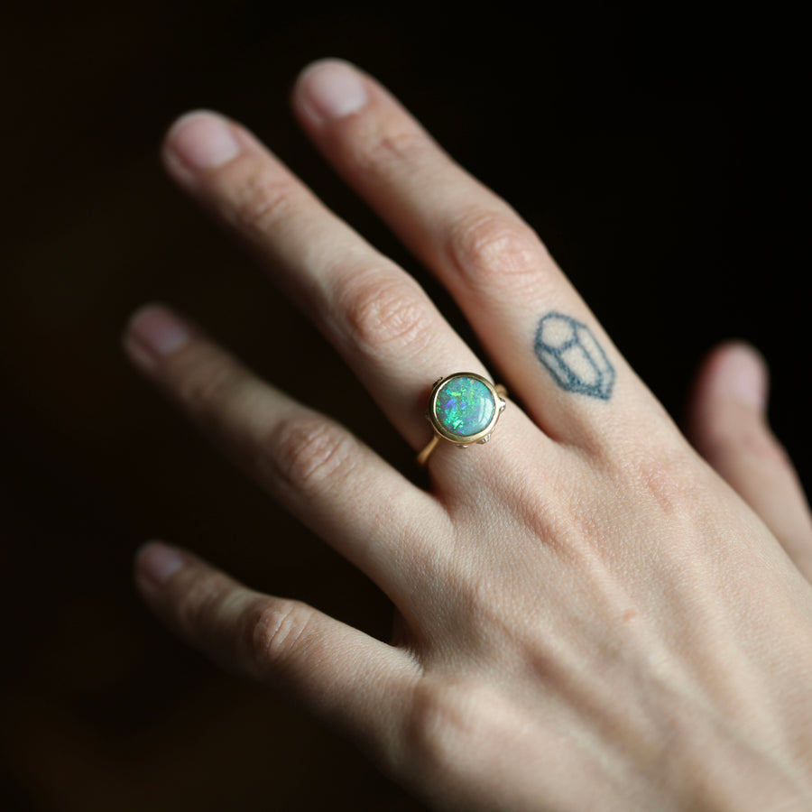 Hand wearing a ring with an opal stone on a dark background