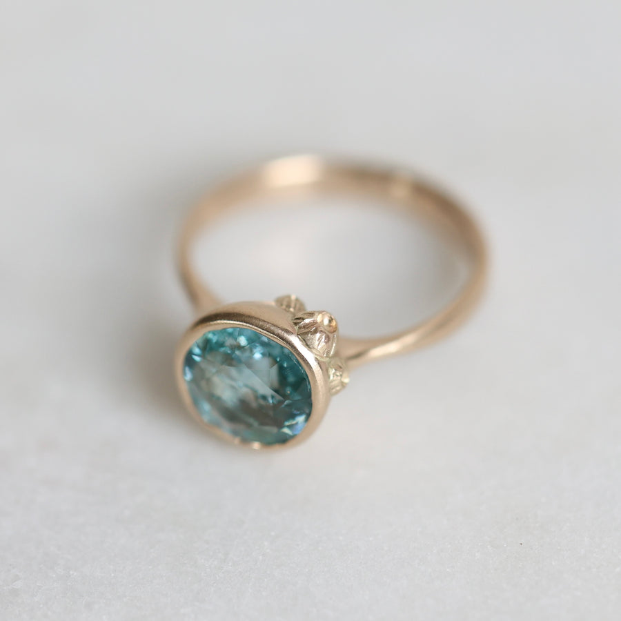 Gold ring with a blue gemstone on a light gray background