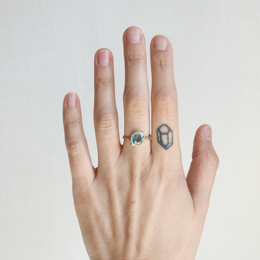 Hand wearing a ring with a blue gemstone on a plain background