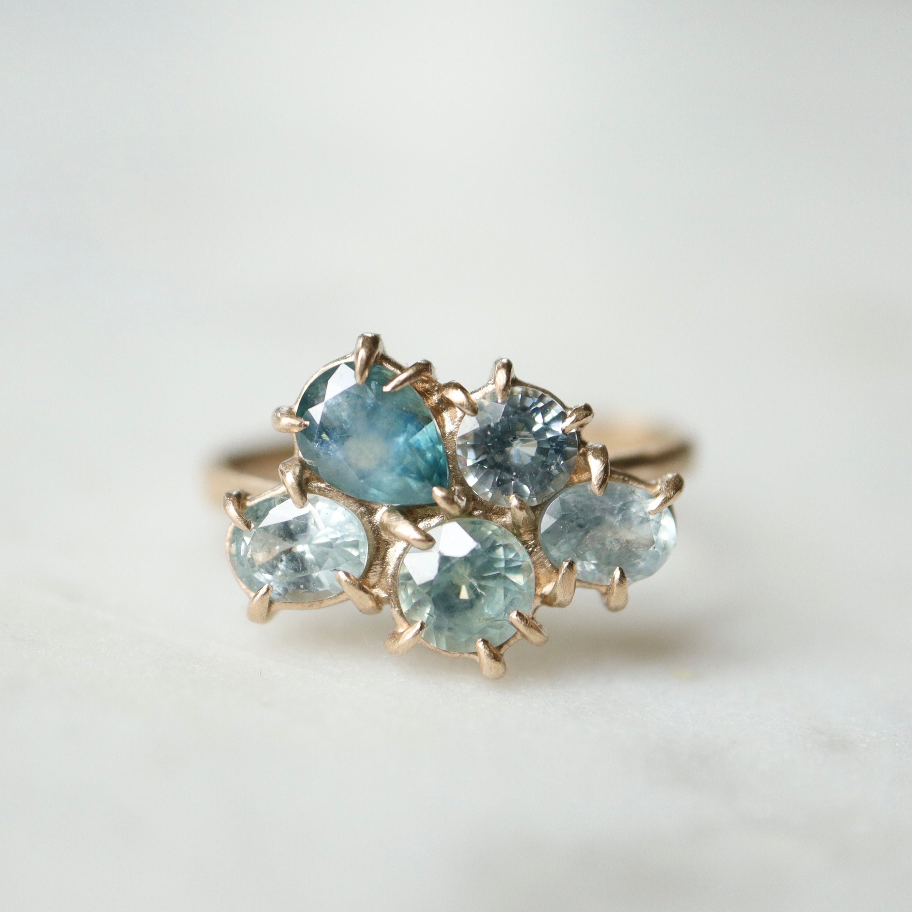 five montana sapphires of various shapes are set in a cluster with gold prongs in a gold ring