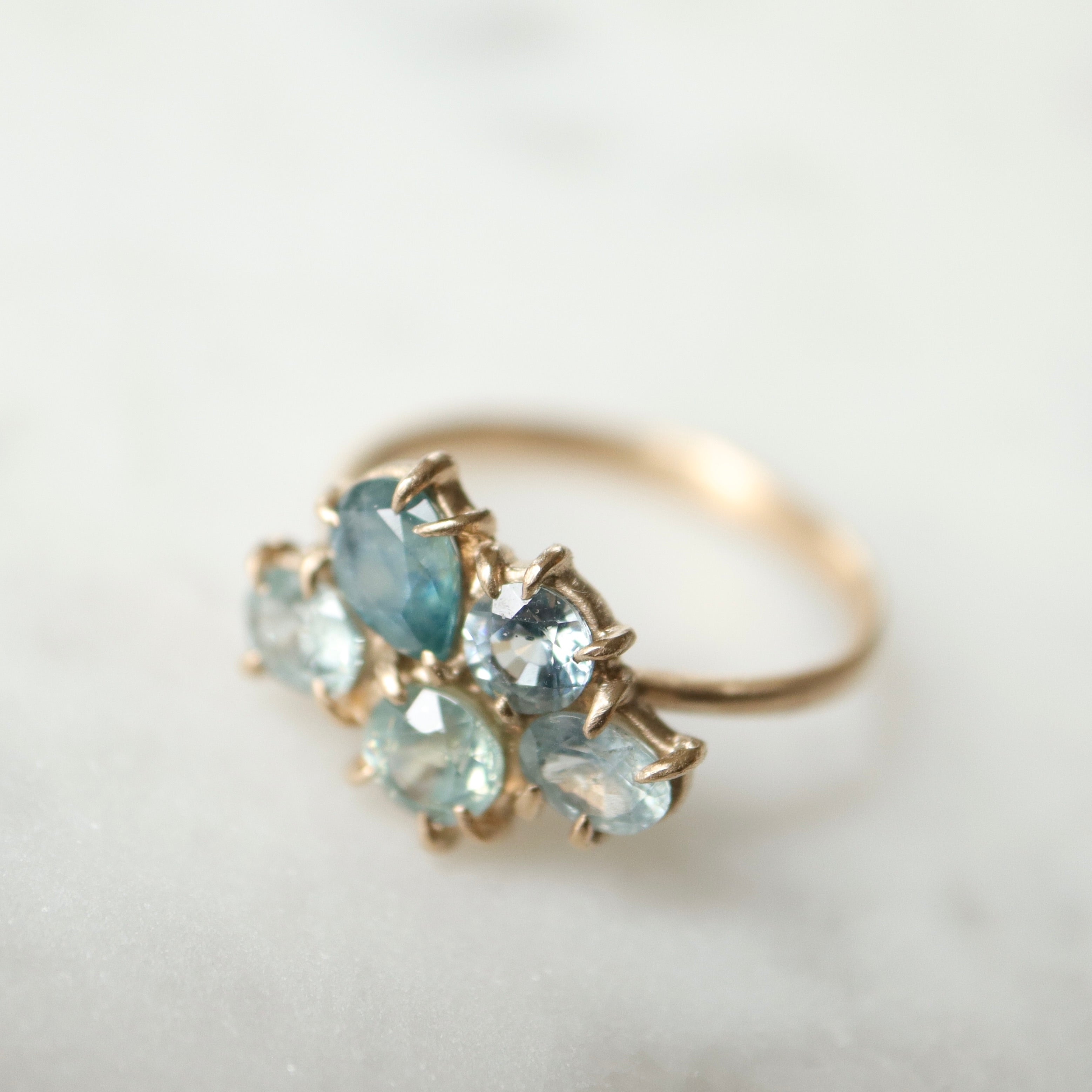 five montana sapphires of various shapes are set in a cluster with gold prongs in a gold ring