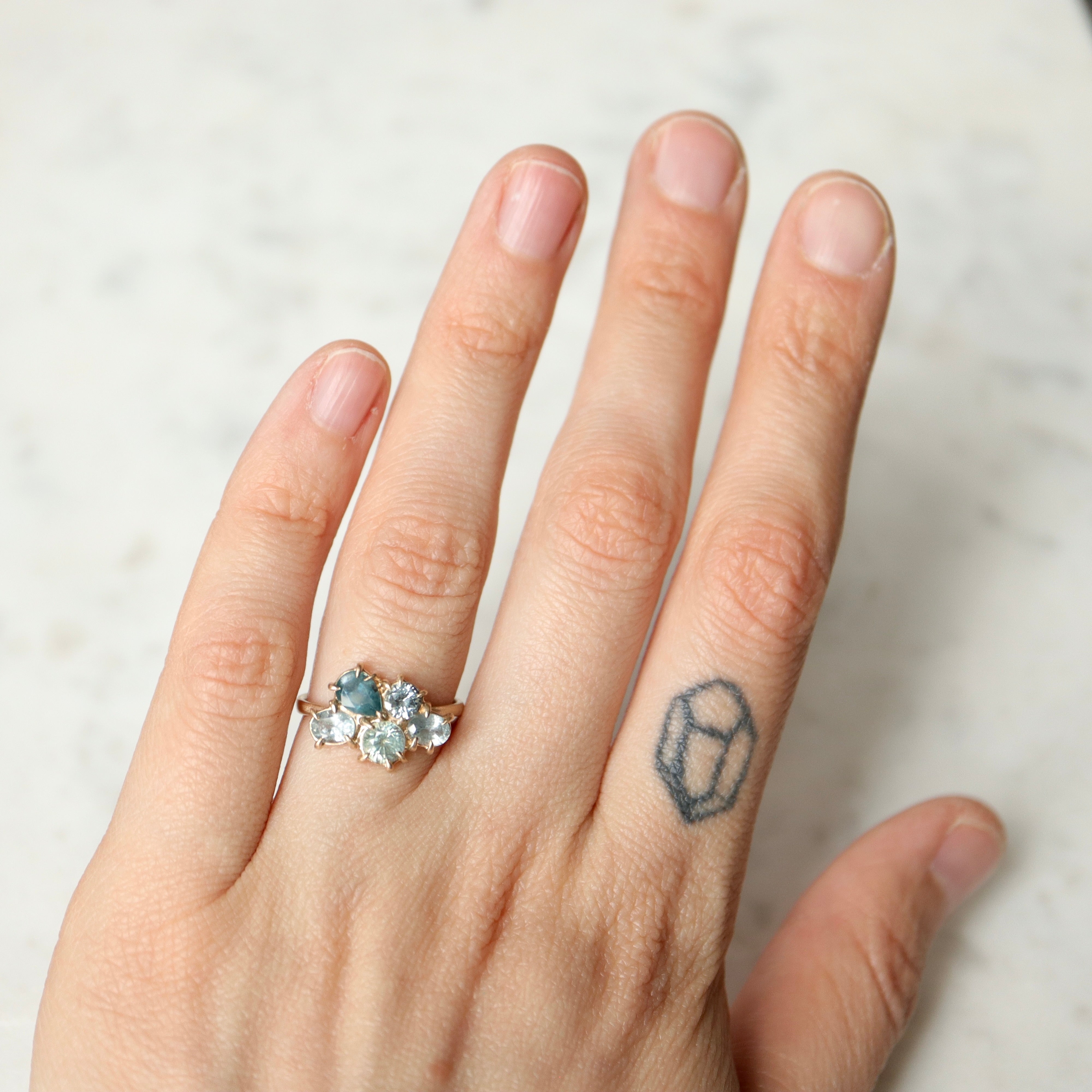 five montana sapphires of various shapes are set in a cluster with gold prongs in a gold ring- on person