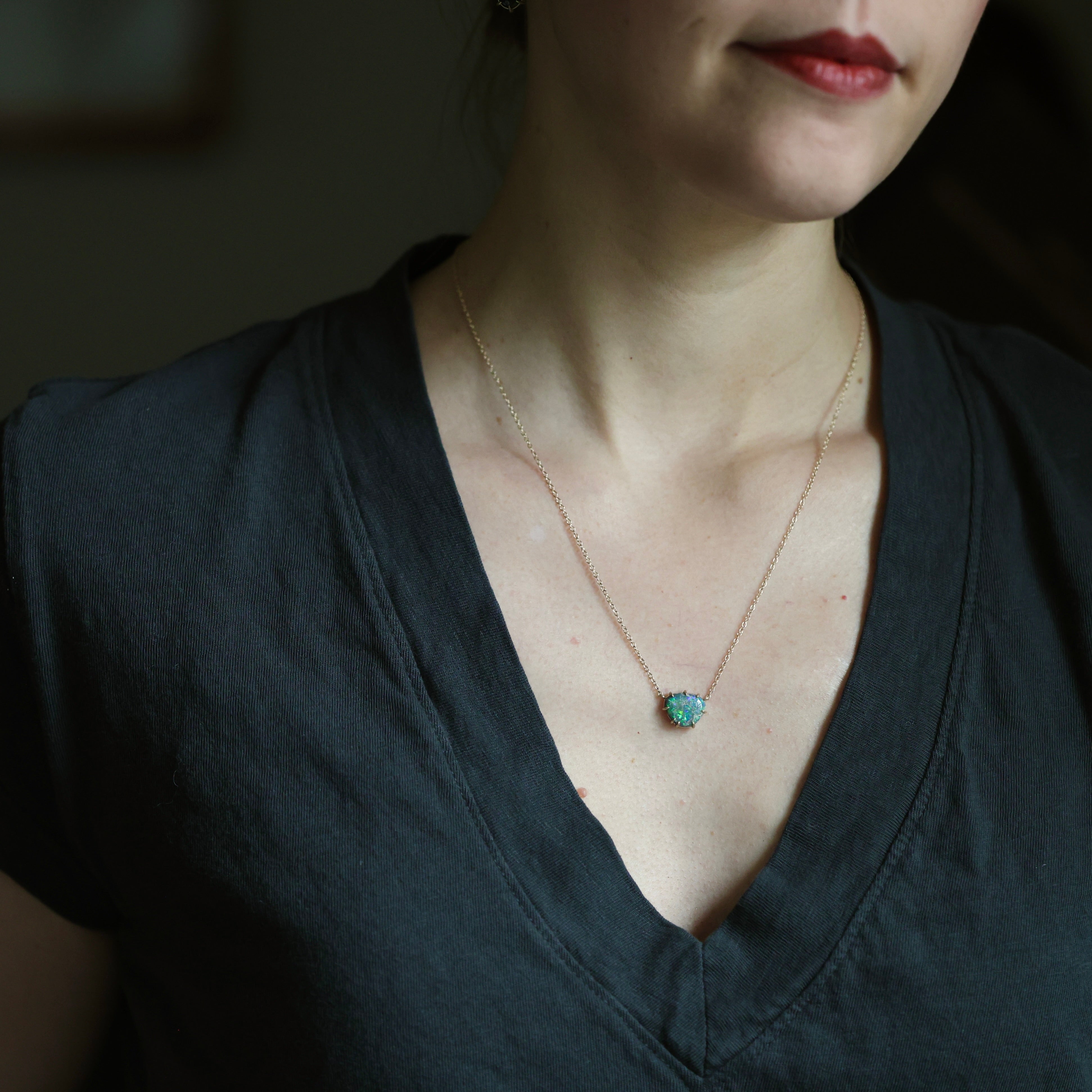 Person wearing a necklace with a green pendant against a dark background