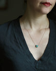 Person wearing a necklace with a green pendant against a dark background