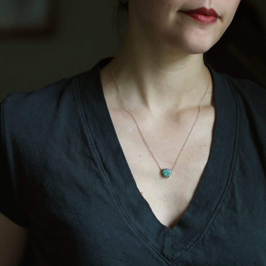 Person wearing a necklace with a green pendant against a dark background