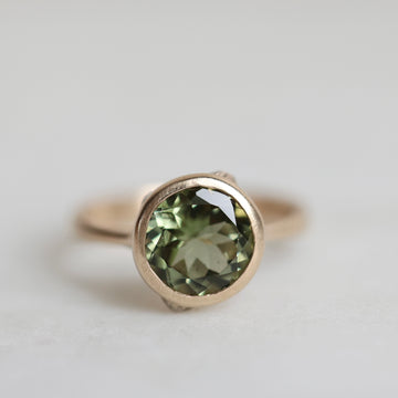 Gold ring with a green gemstone on a light gray background