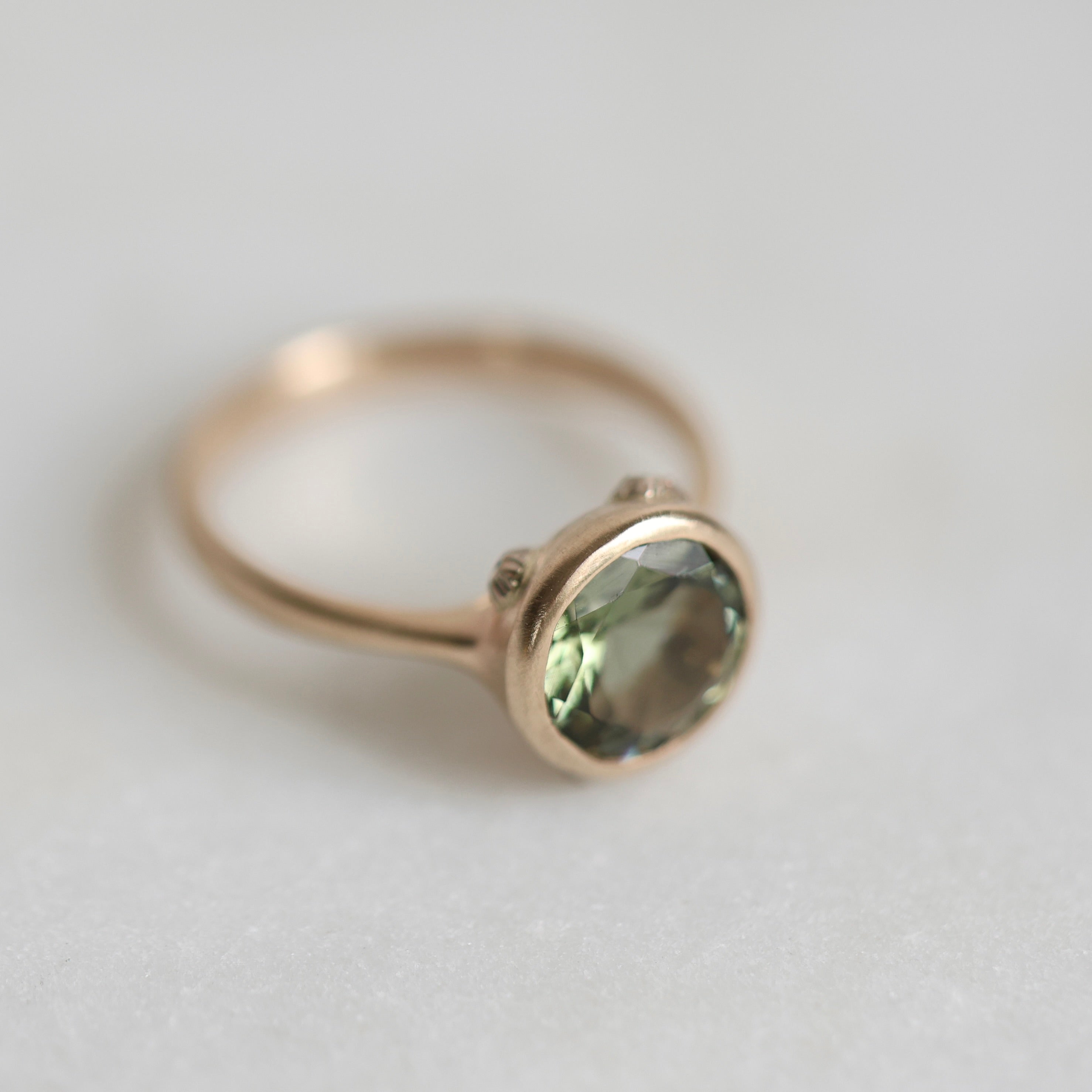 Gold ring with a green gemstone on a light gray background