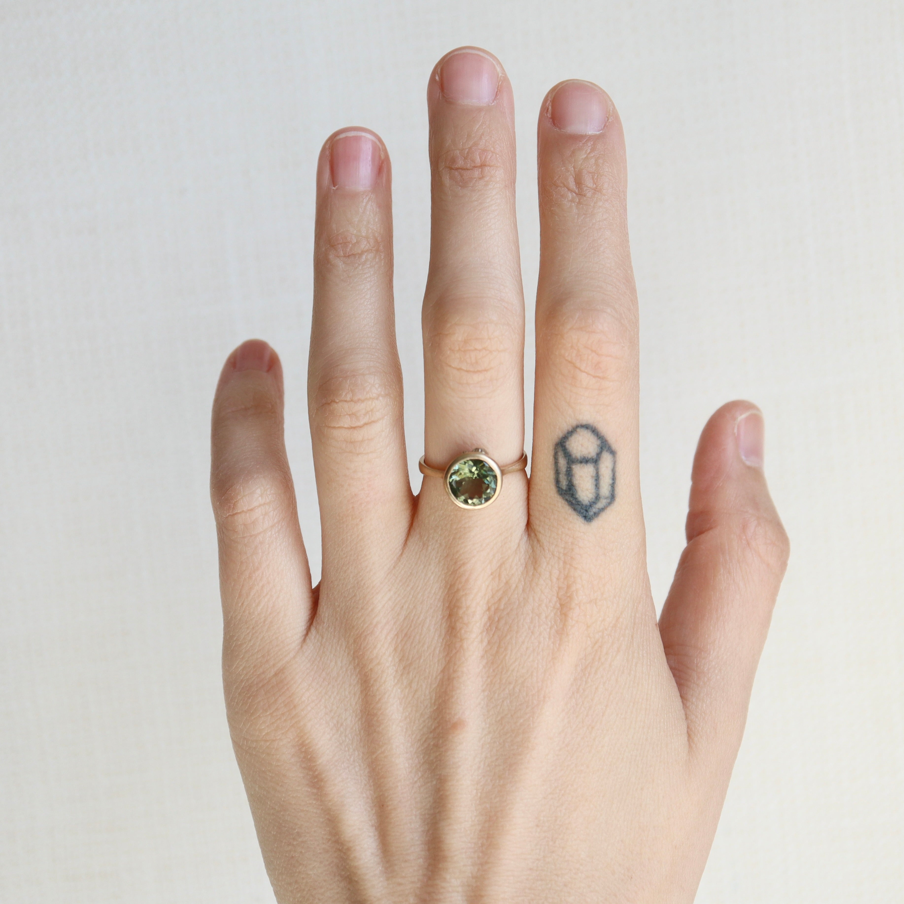 Hand wearing a gold ring with a green gemstone on a plain background
