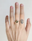 Hand wearing a gold ring with a green gemstone on a plain background