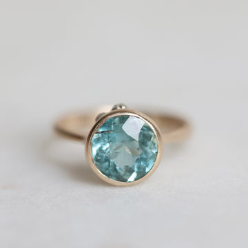 Gold ring with a blue gemstone on a light gray background