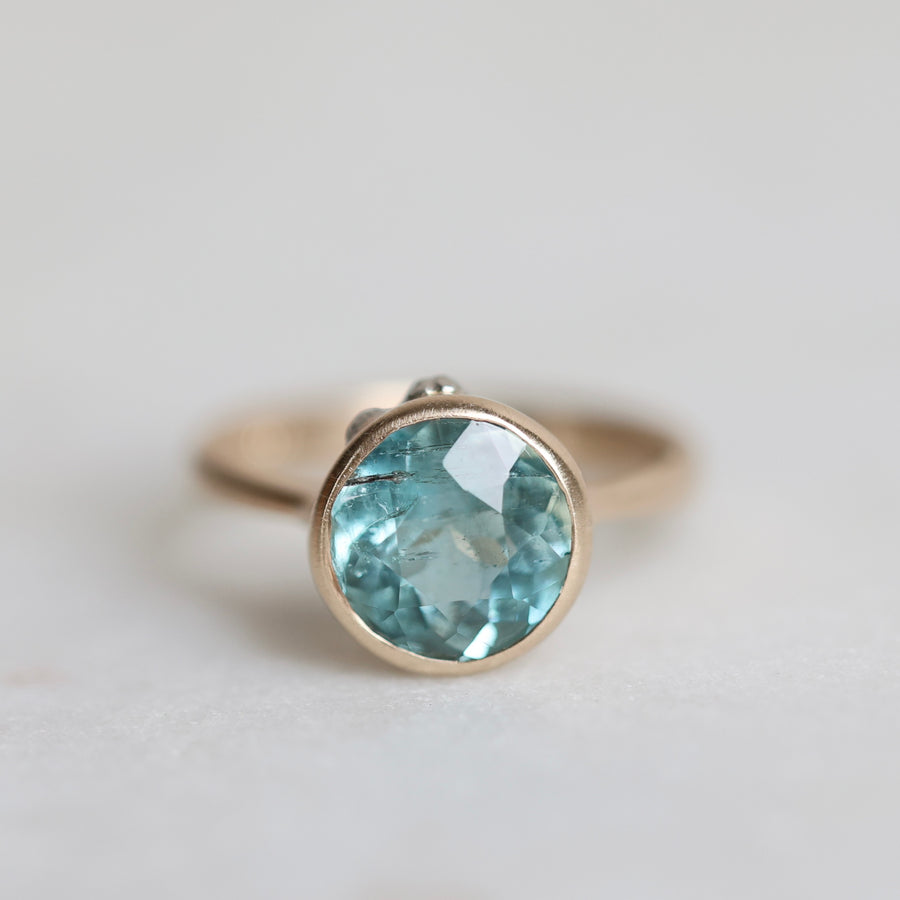 Gold ring with a blue gemstone on a light gray background