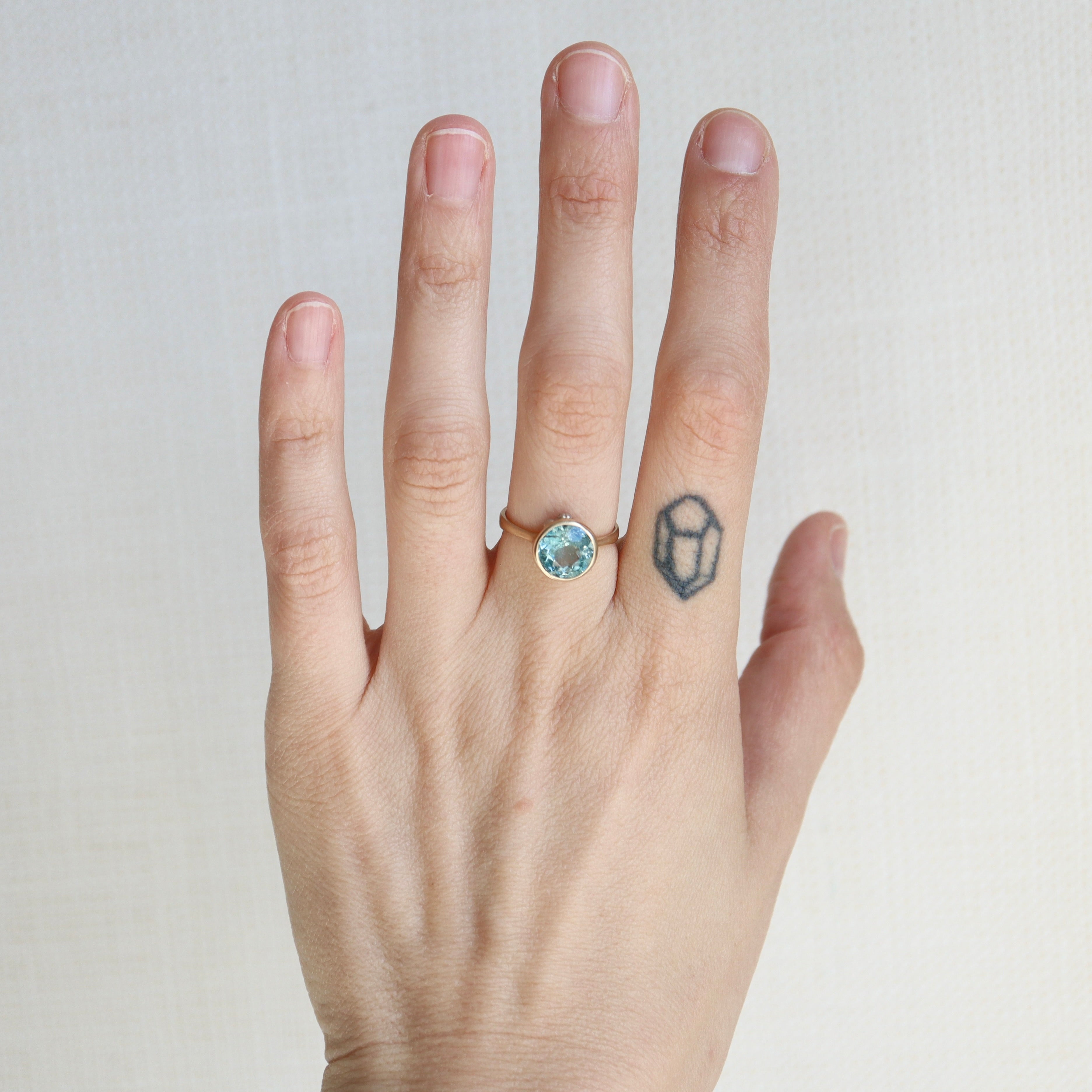 Hand wearing a ring with a blue gemstone on a plain background