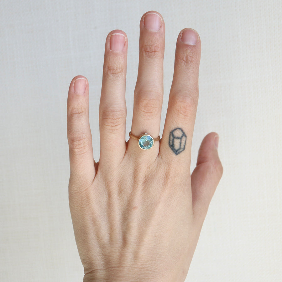 Hand wearing a ring with a blue gemstone on a plain background