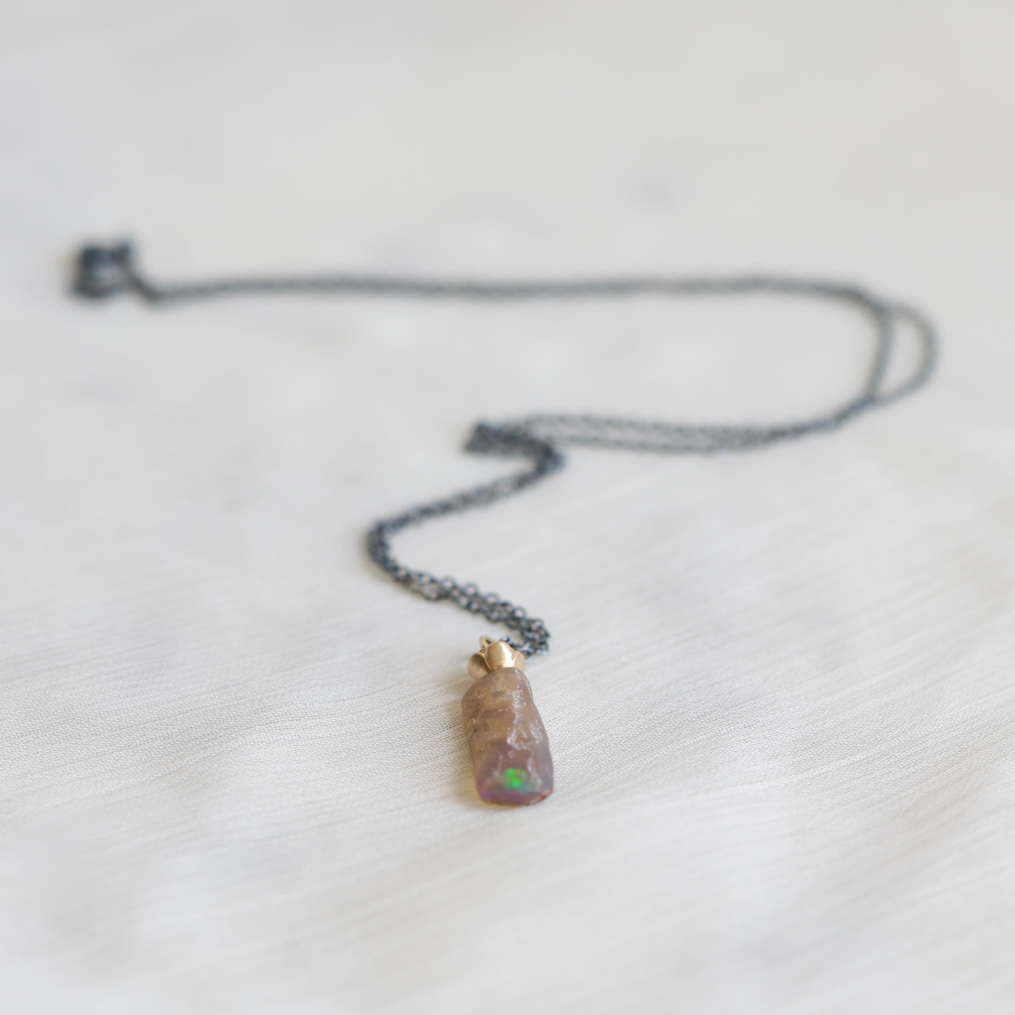 Necklace with an amber colored opal  with a flash of green on a light gray background