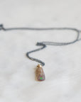 Necklace with an amber colored opal  with a flash of green on a light gray background