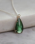 Teardrop-shaped green gemstone pendant on a silver chain against a marble background