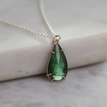 Teardrop-shaped green gemstone pendant on a silver chain against a marble background