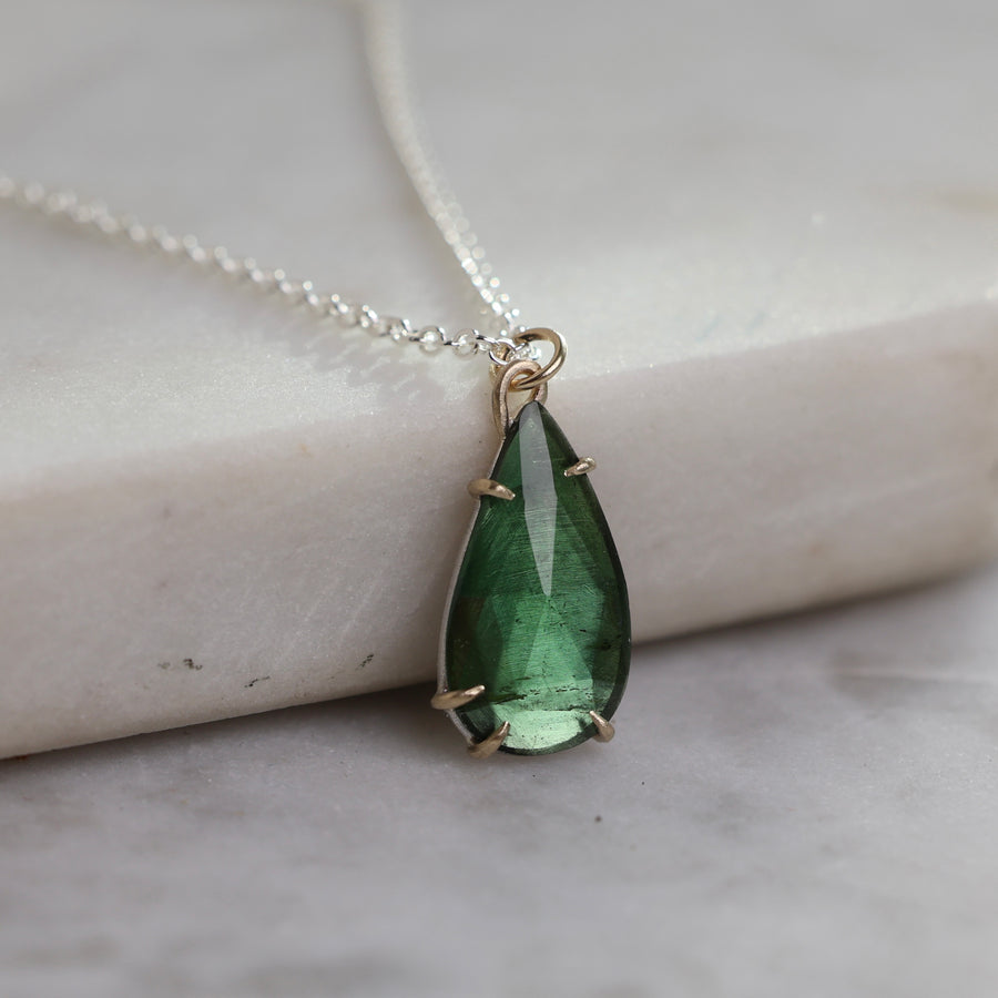 Teardrop-shaped green gemstone pendant on a silver chain against a marble background