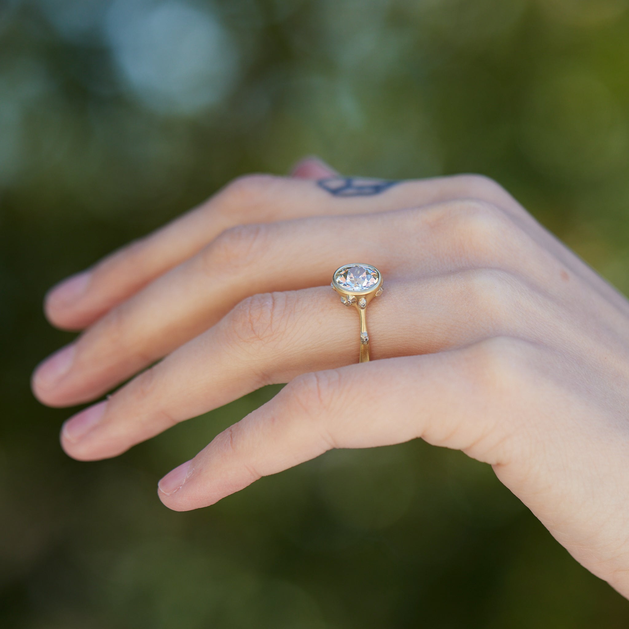 Diamond ring with gold bezel setting and white gold barnacles. THe barnacles have diamonds in them. On person.