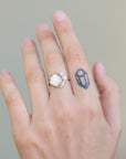 Hand wearing a ring with a large gemstone on a neutral background