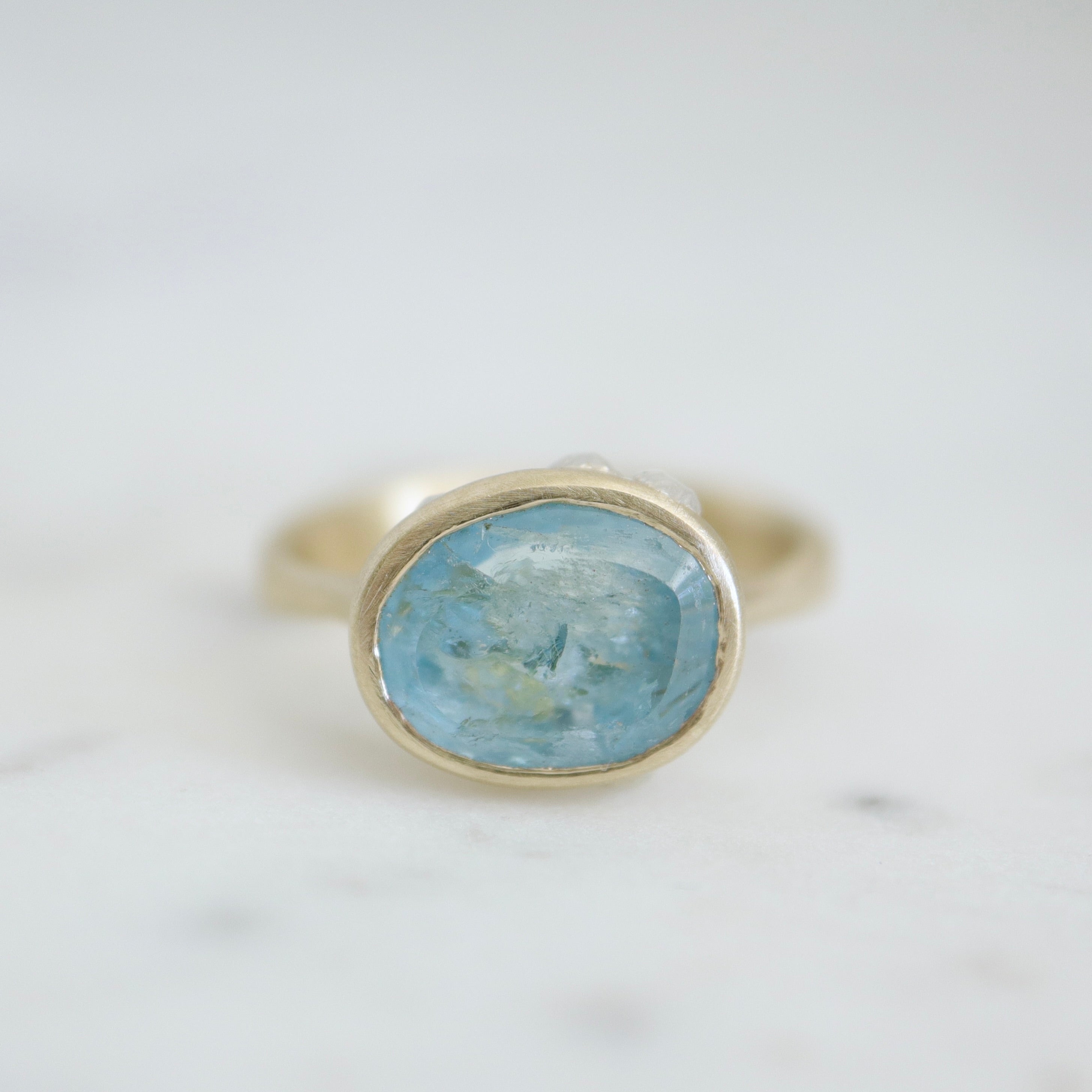 An oblong faceted aquamarine is set in a gold band with little silver barnacles around the setting. Front view.