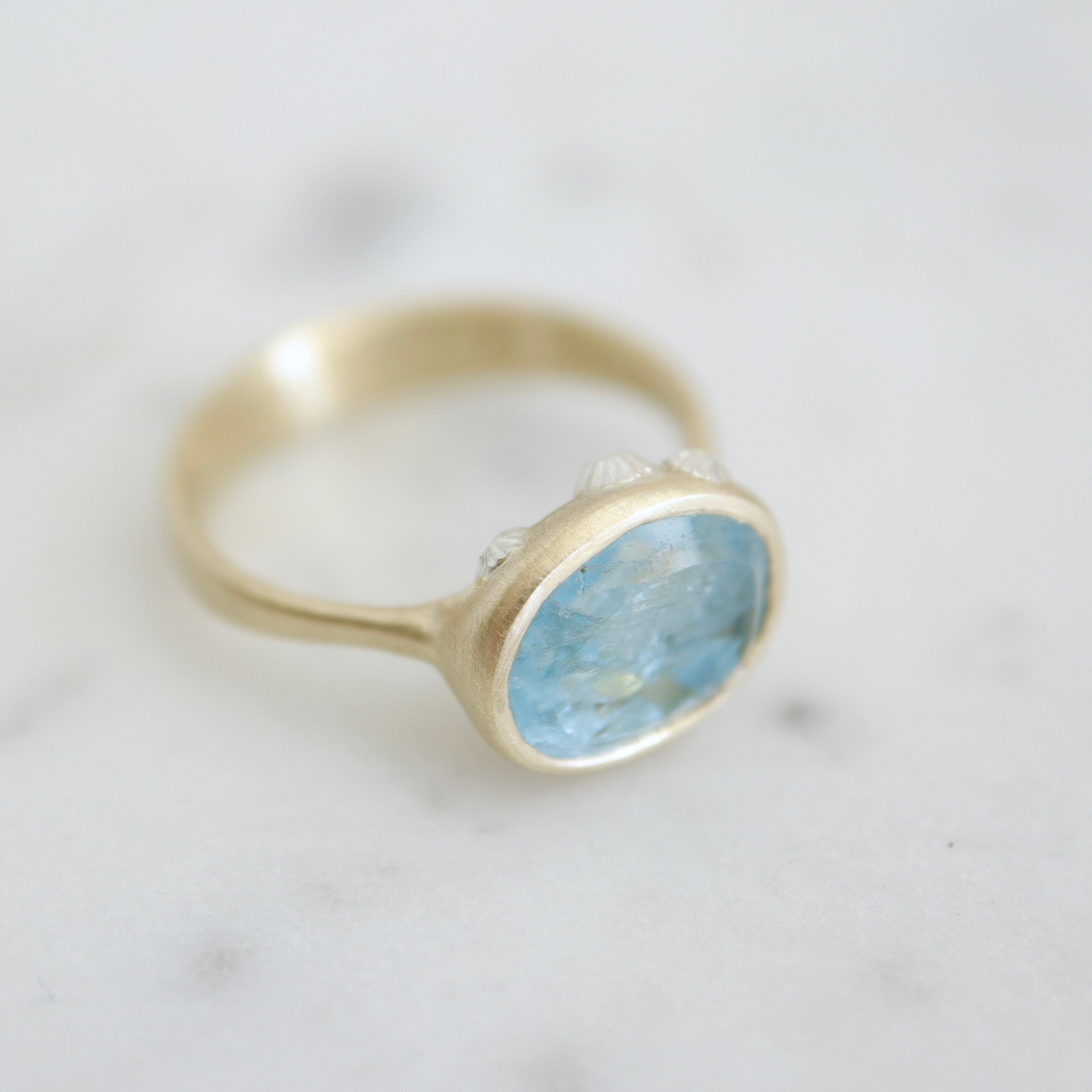 An oblong faceted aquamarine is set in a gold band with little silver barnacles around the setting. 1/4 view.