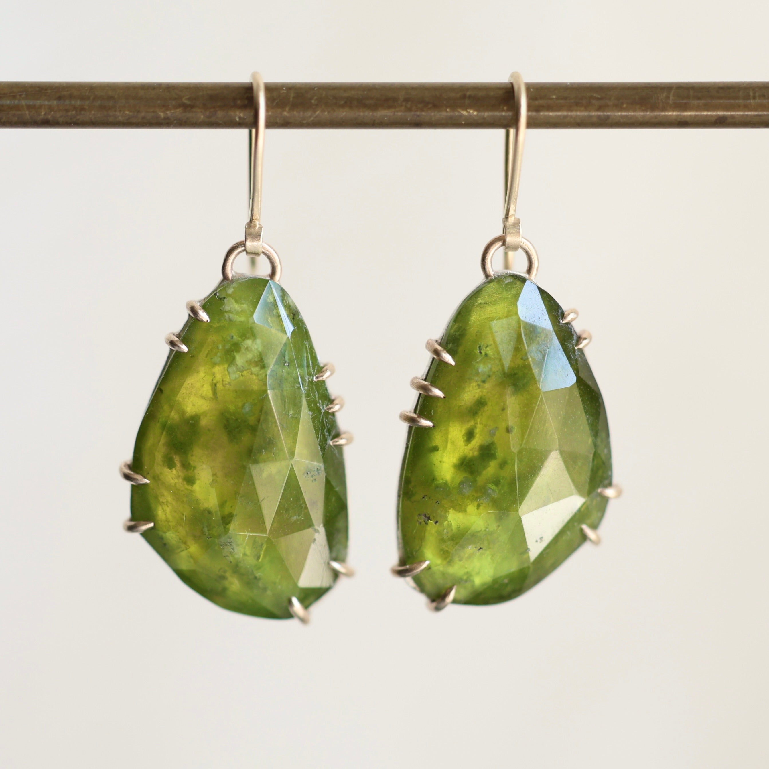 Green teardrop earrings with gold accents on a white background